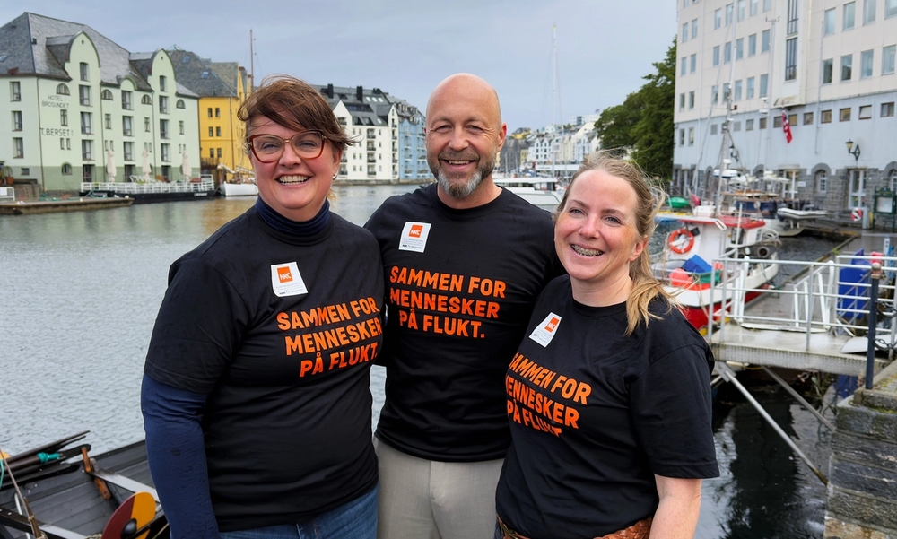 Tre mennesker med svarte tskjorter med oransje tekst som smiler mot kamera.