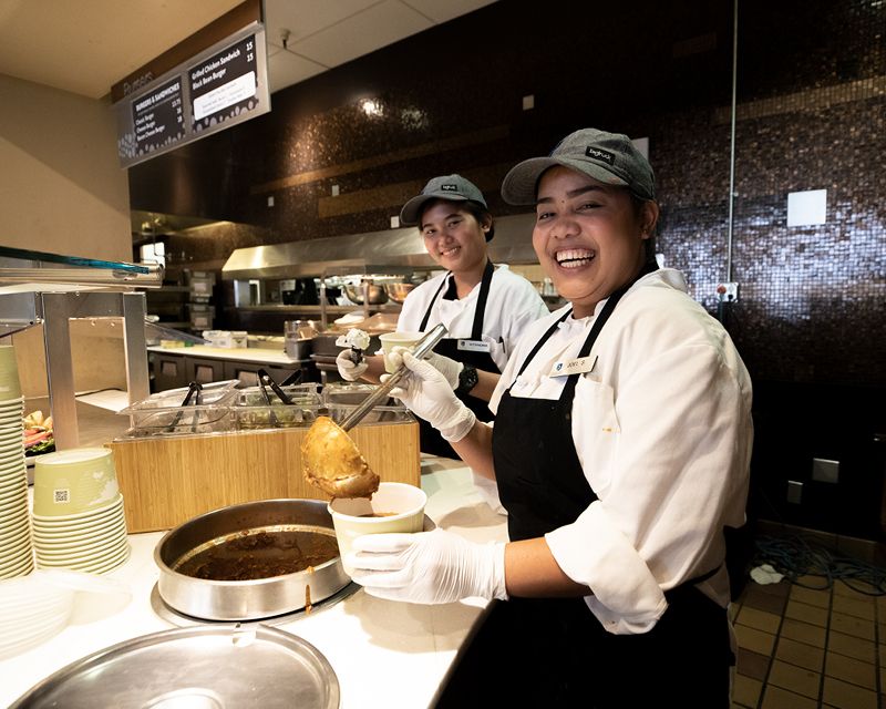Two people filling cups of soup and smiling at the camera