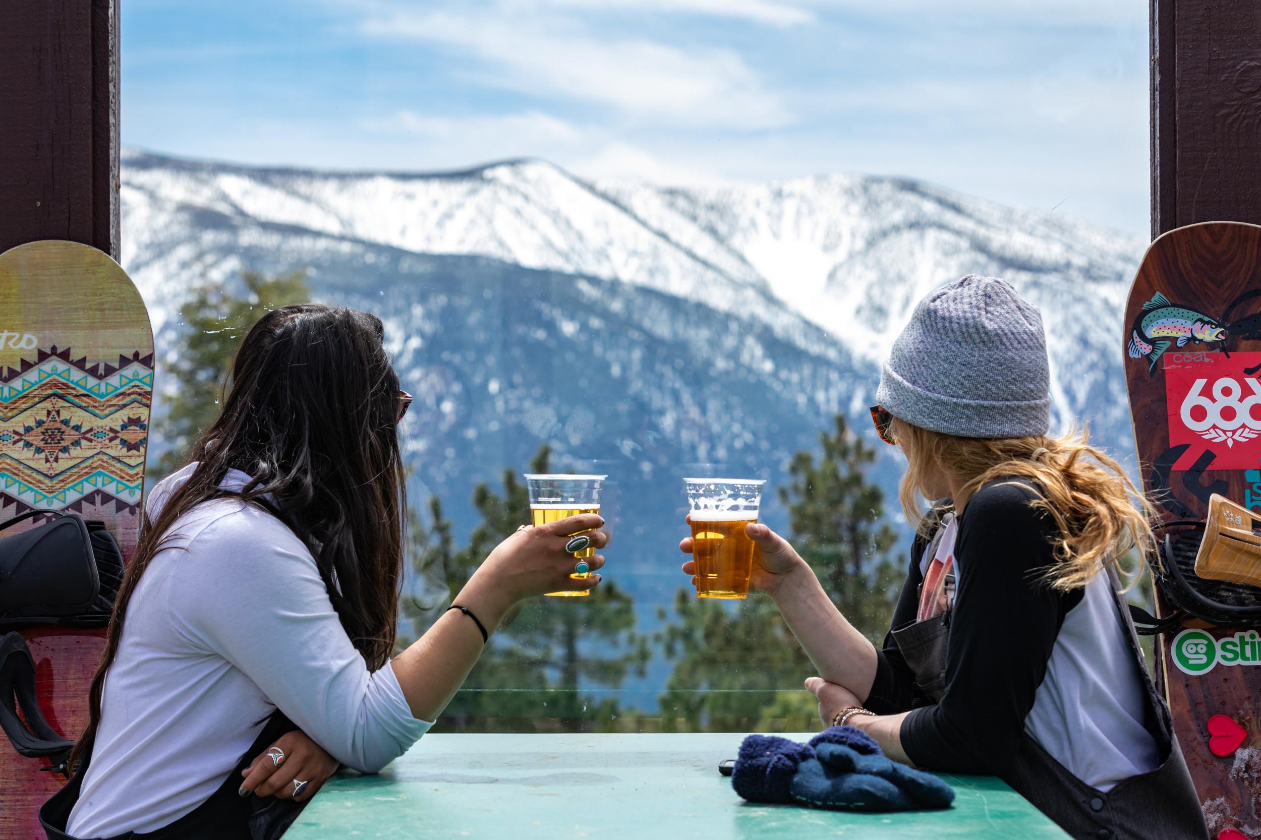 Two people sitting at a table holding beers looking at the mountain view