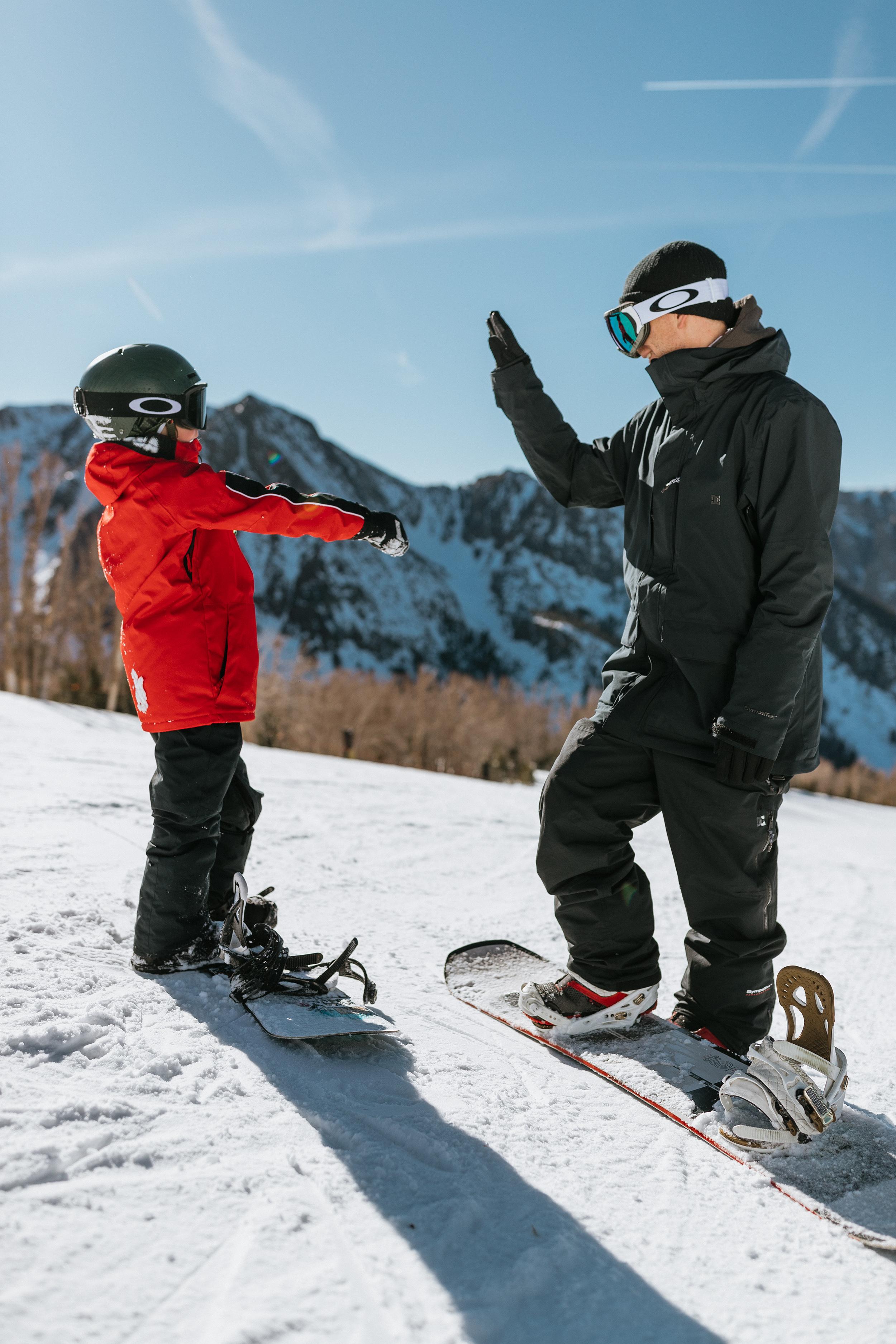 An adult and kid on snowboards giving each other a high five