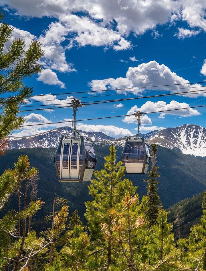 Scenic image of gondolas during the summer with a snowcapped mountain in the background.