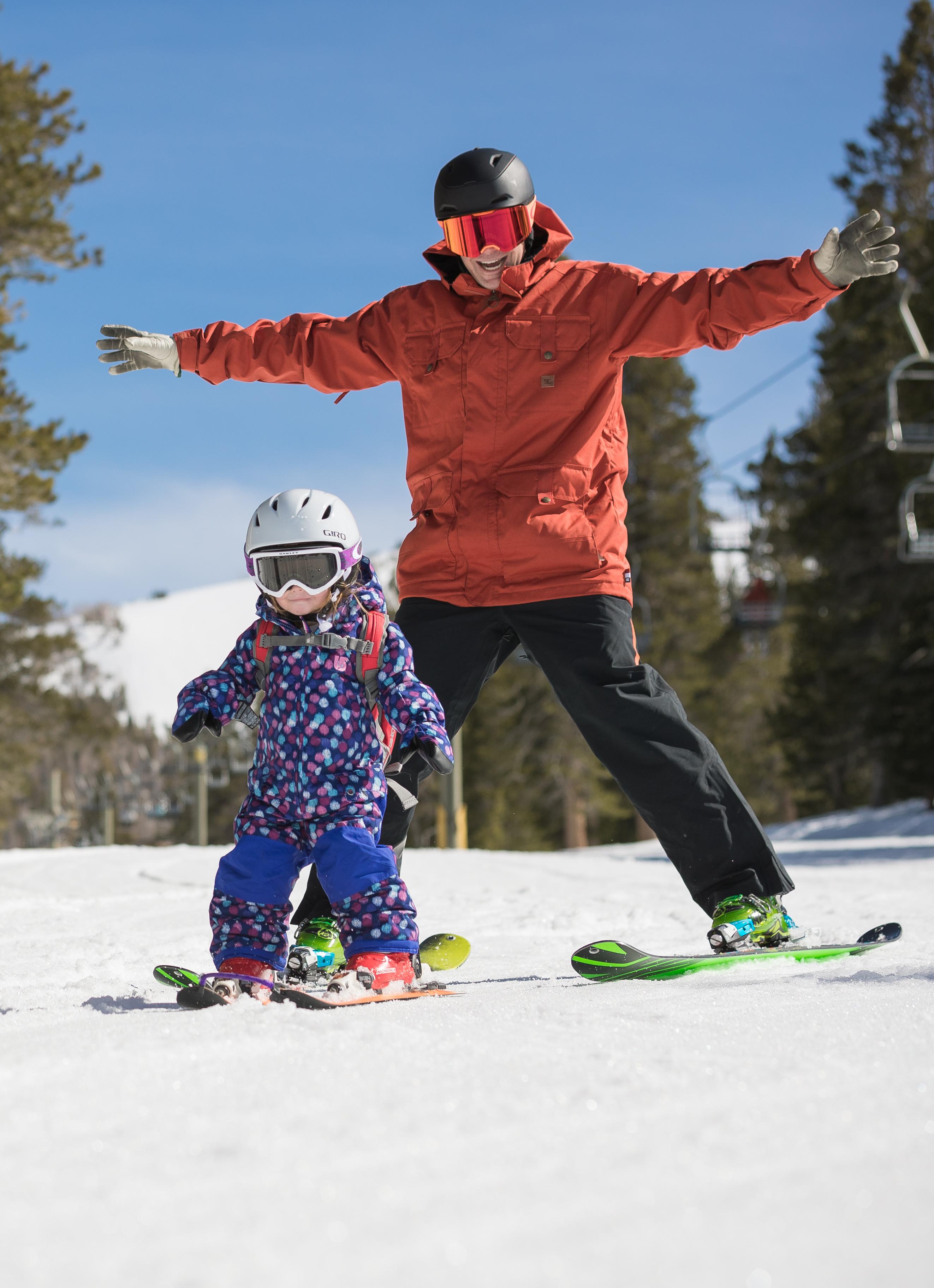 An adult skiing behind a child also on skis