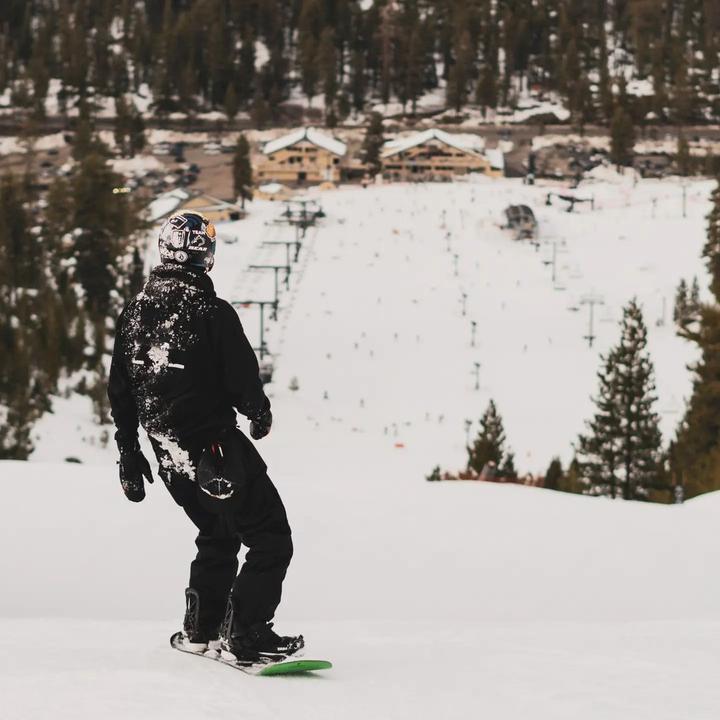 Snowboarder going down a ski hill with the base of the resort in the background