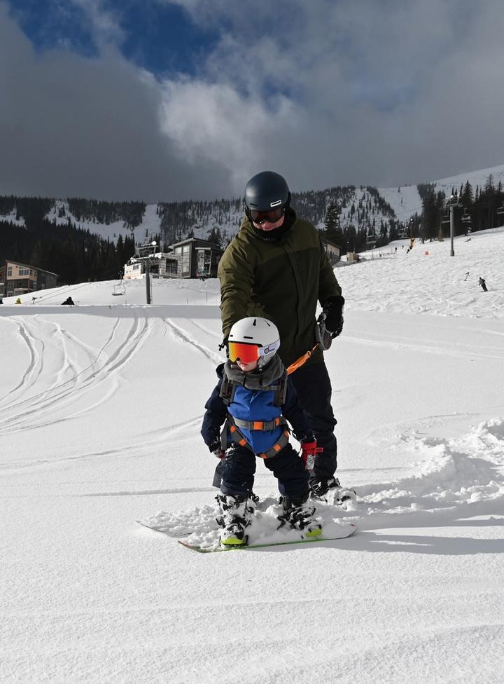 Adult on a snowboard helping a child on a snowboard