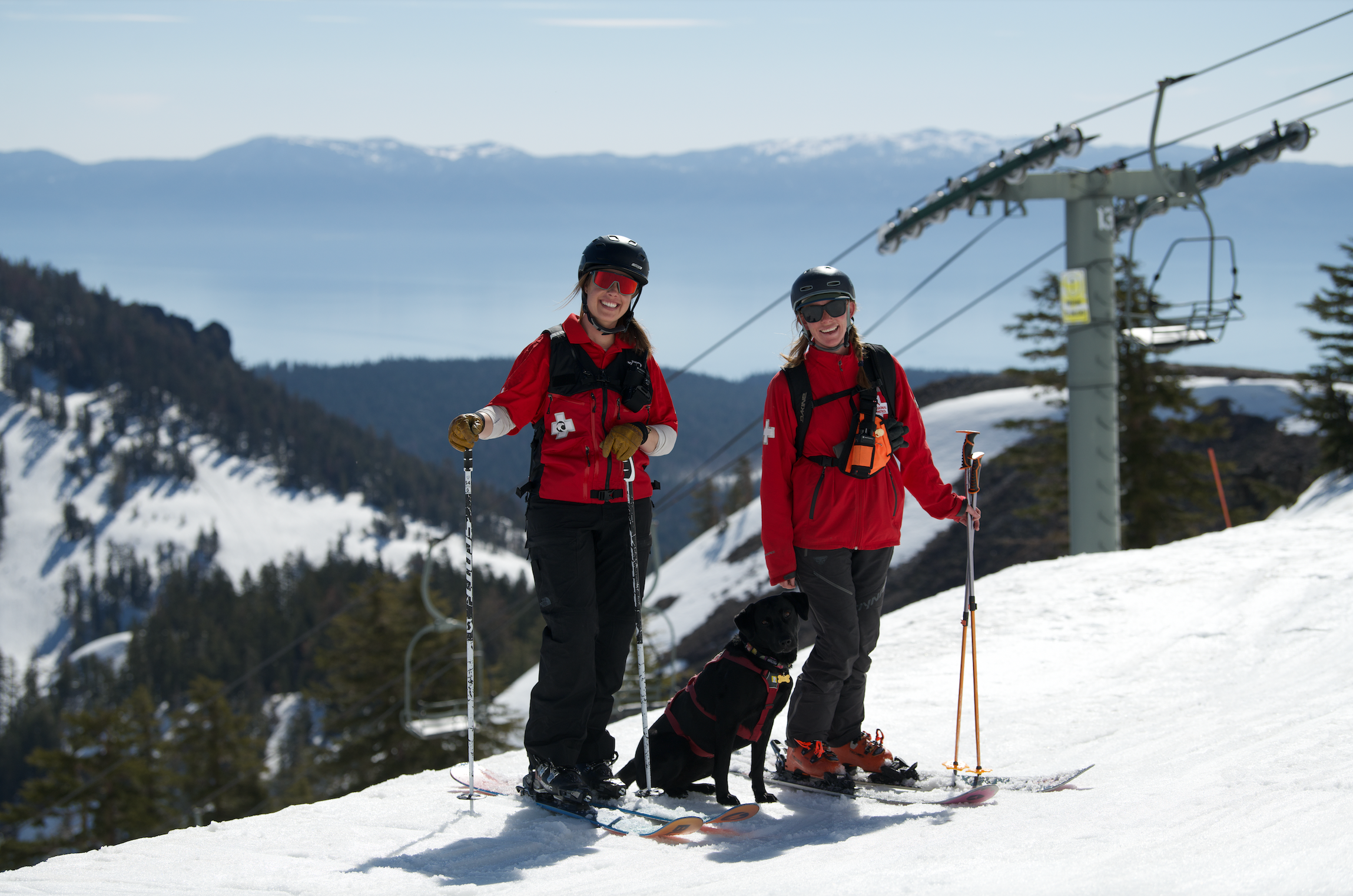 Two ski patrol members and an avalanche dog standing on a trail.
