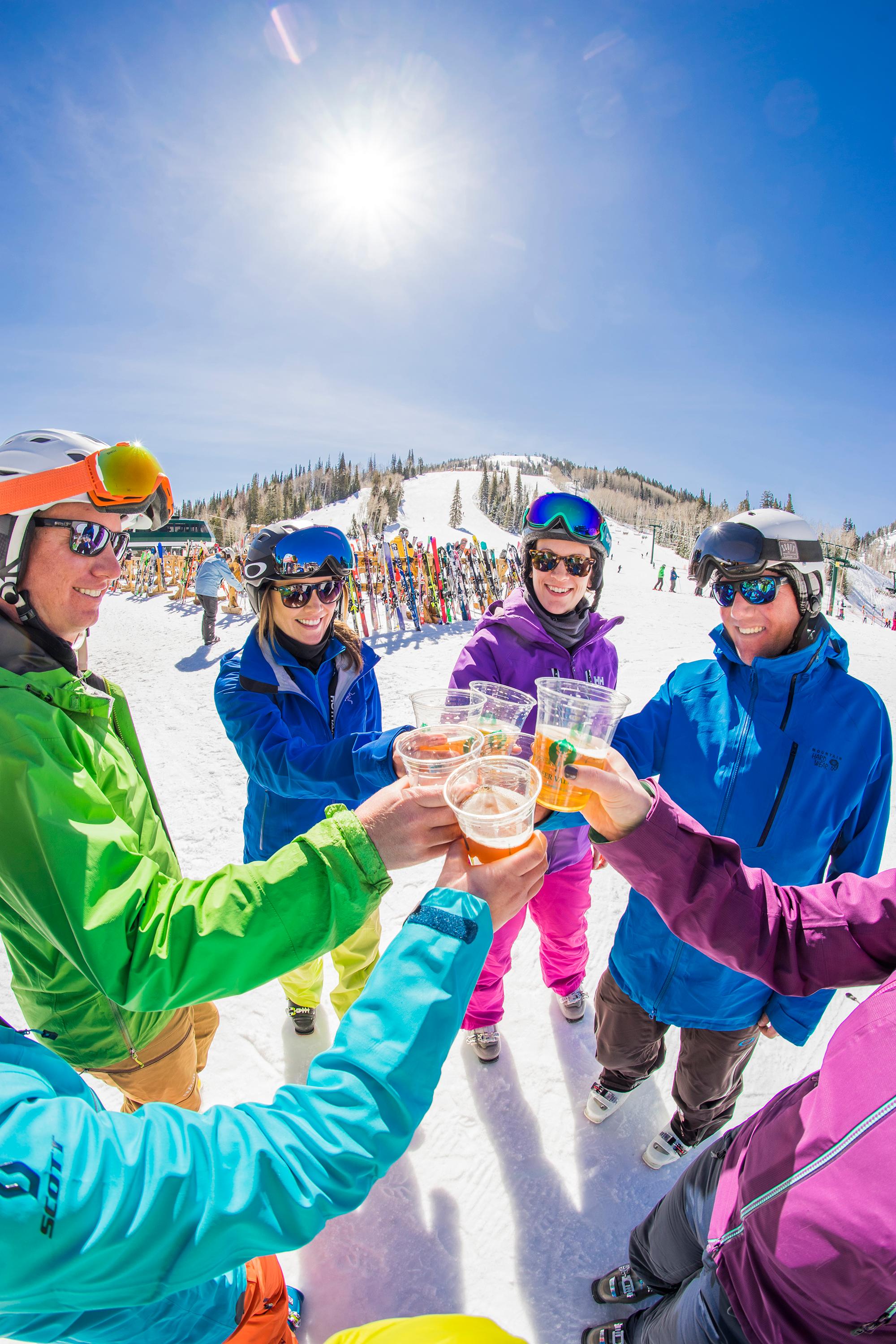 Group of people in ski gear toasting with beers at the base of a mountain