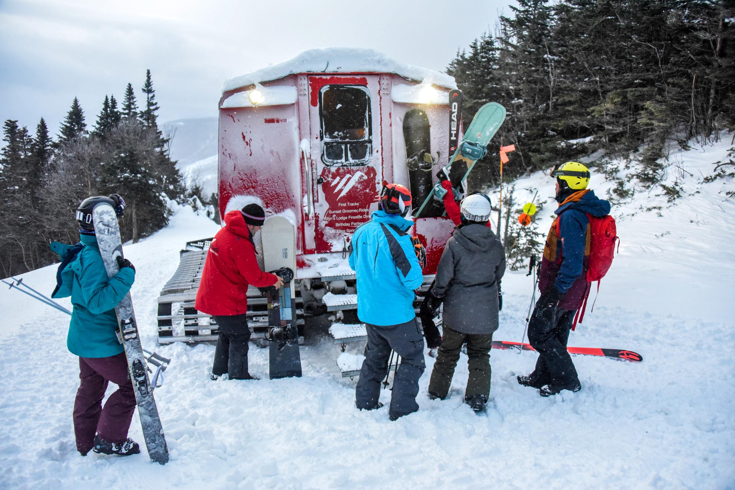 People in winter gear carrying skis and snowboards next to a snowcat
