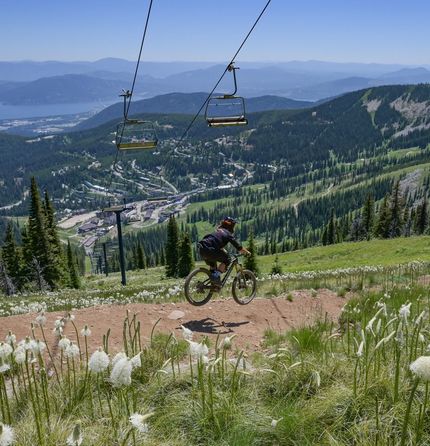Person mountain biking with a ski lift in the background and a mountain lake in the distance