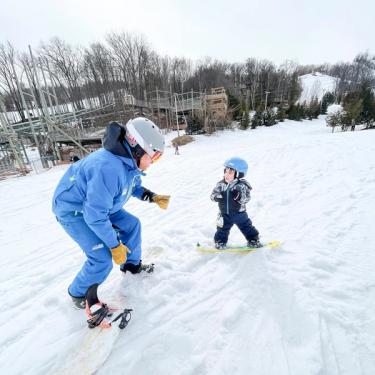 Adult snowboarding instructor showing a child how to snowboard