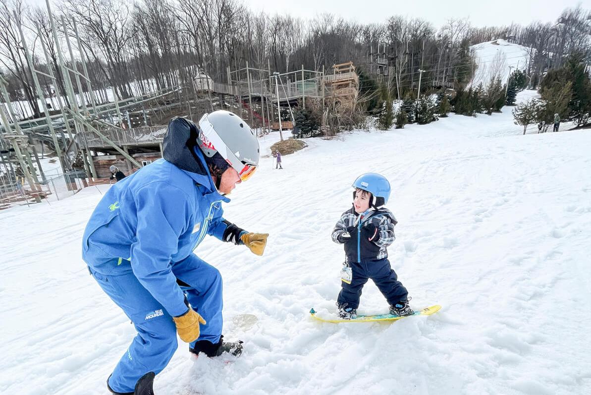 Adult snowboarding instructor showing a child how to snowboard