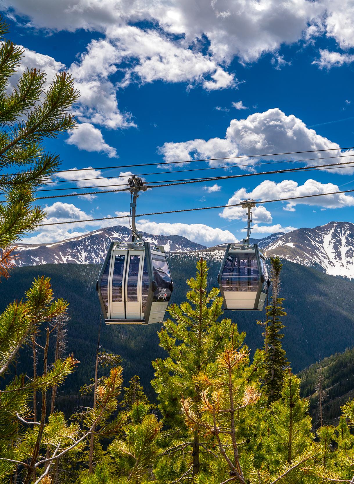 Two gondola cars hanging with snow-covered peaks in the distance