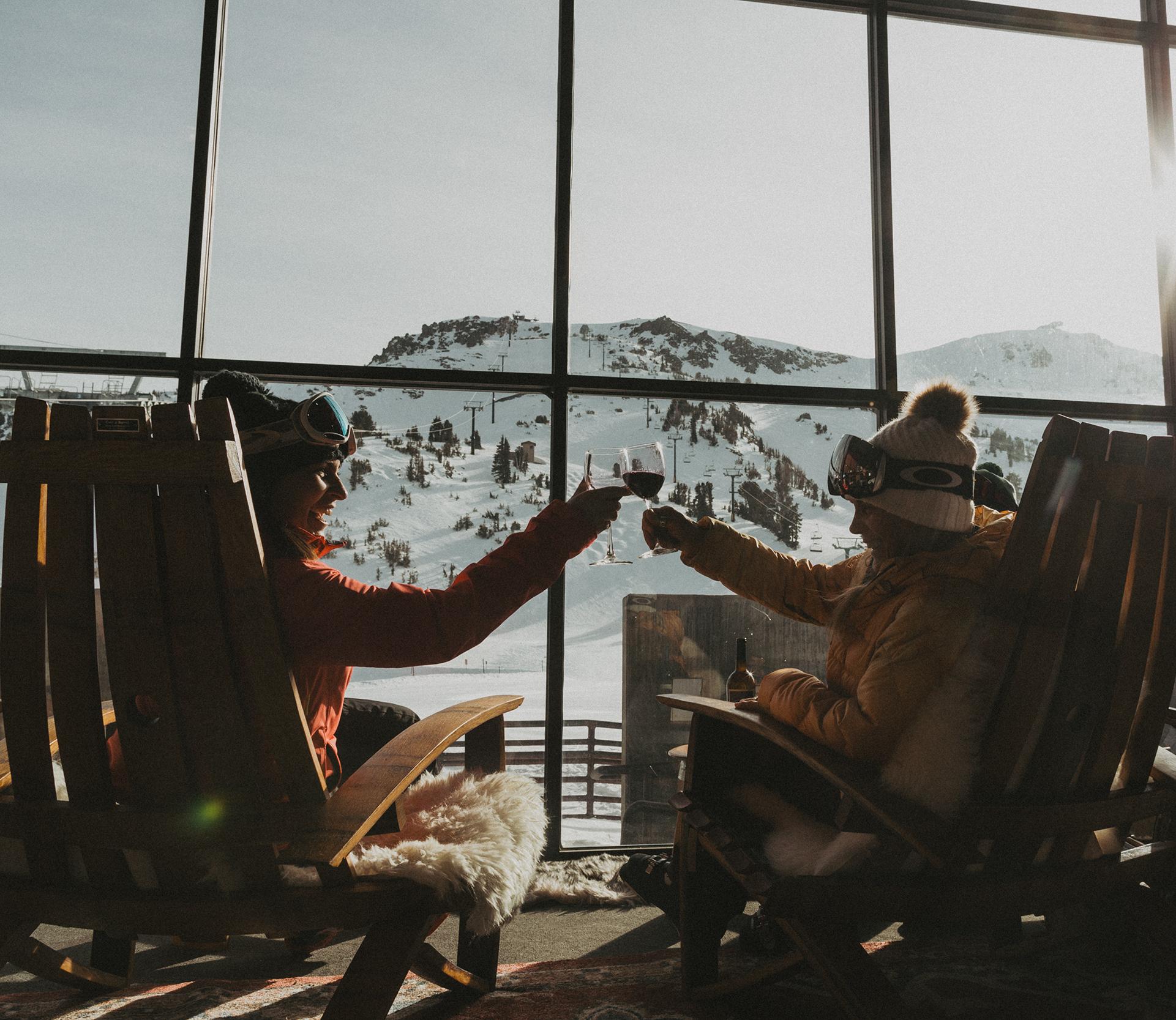 two people sitting in chairs toasting glasses of wine with mountain views out the window