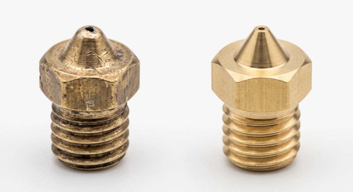 Macro comparison of a worn brass 3D printer nozzle next to a new one
