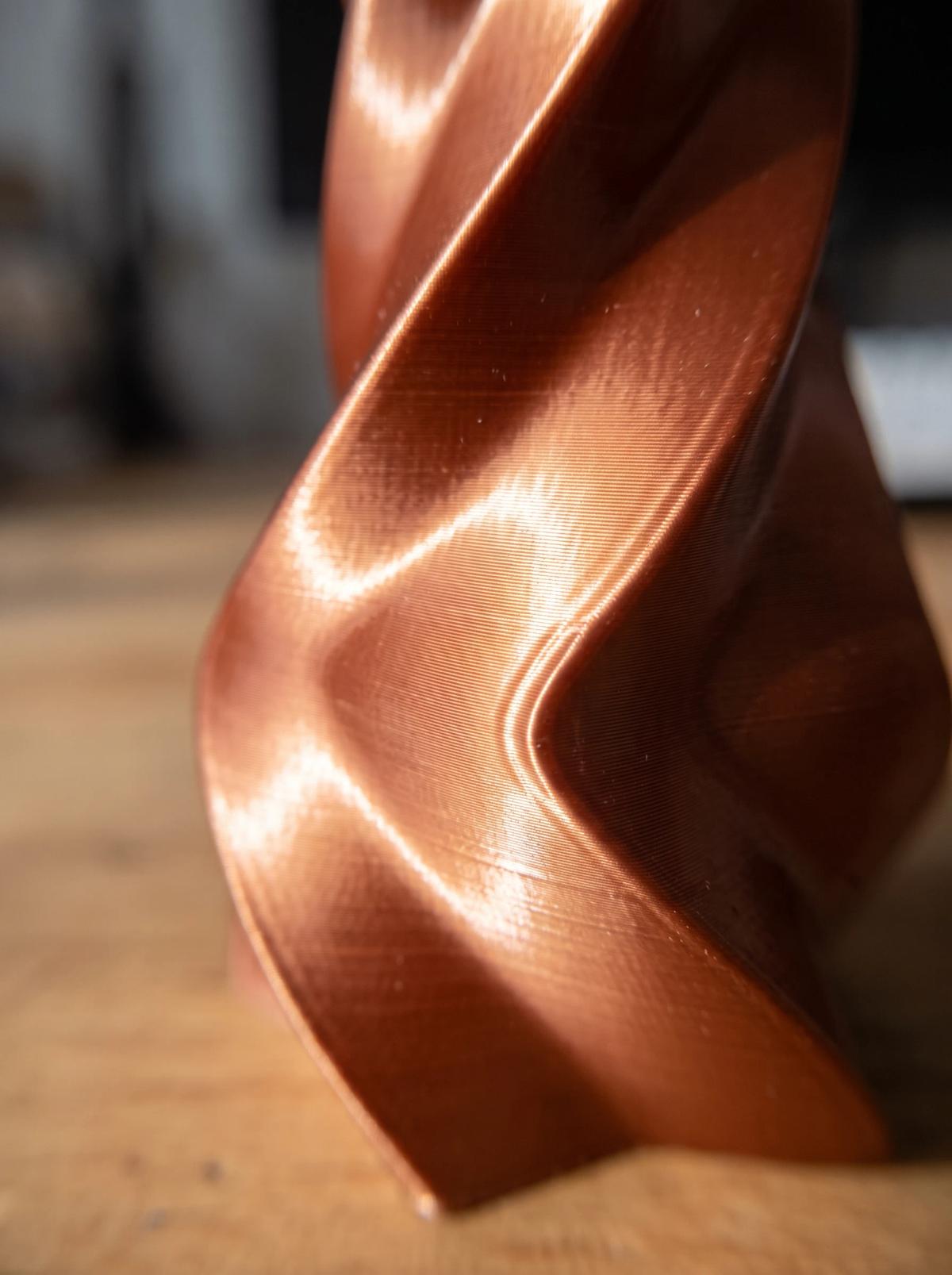 Macro close-up of a glossy copper silk PLA vase, where the reflective finish makes every layer line and small surface unevenness visible