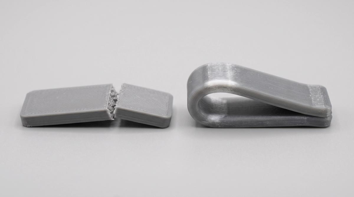 Two 3D printed test strips after a bending test, the PLA strip snapped in two and the PETG strip bent into a U-shape but still in one piece