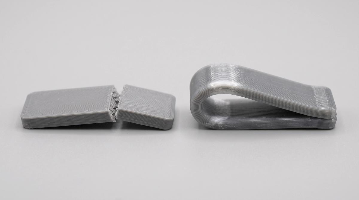 Two 3D printed test strips after a bending test, the PLA strip snapped in two and the PETG strip bent into a U-shape but still in one piece