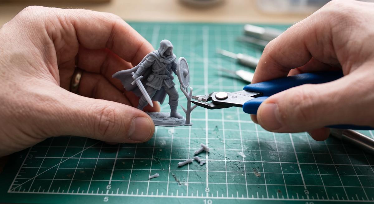 Flush cutters clipping a support structure off a grey 3D printed miniature over a cutting mat