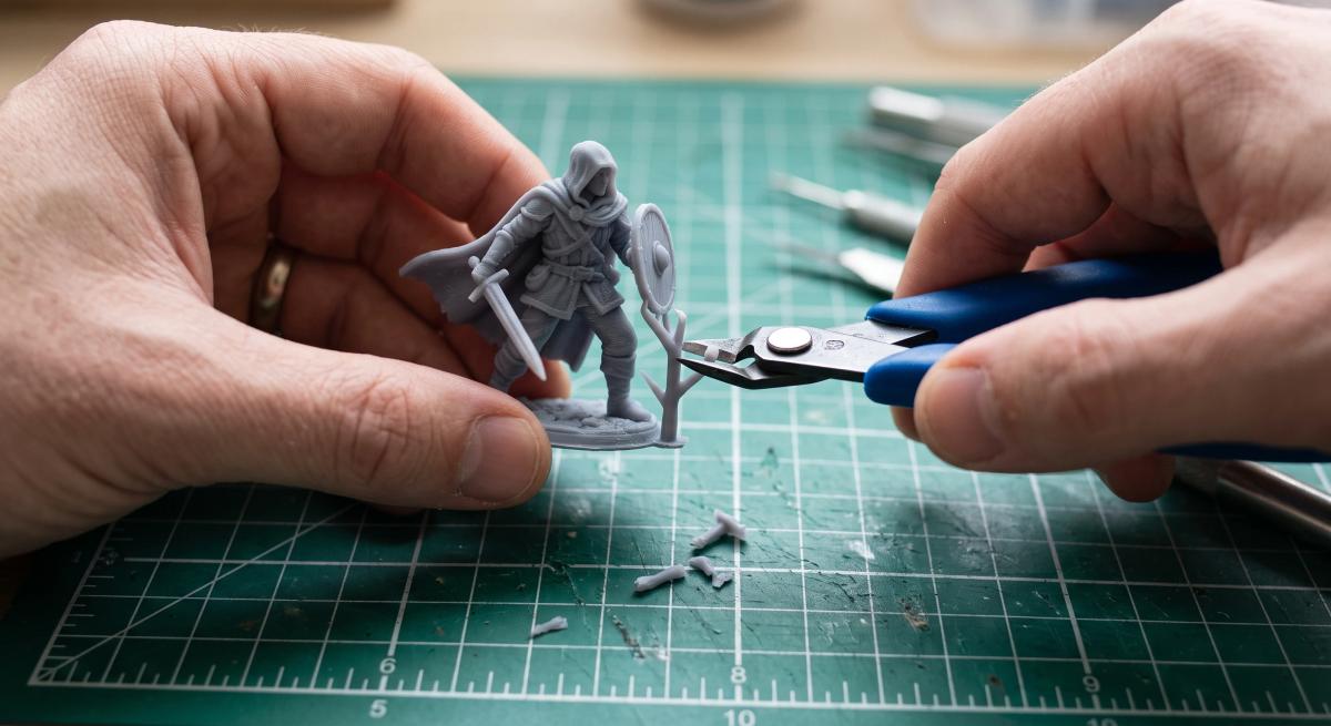 Flush cutters clipping a support structure off a grey 3D printed miniature over a cutting mat