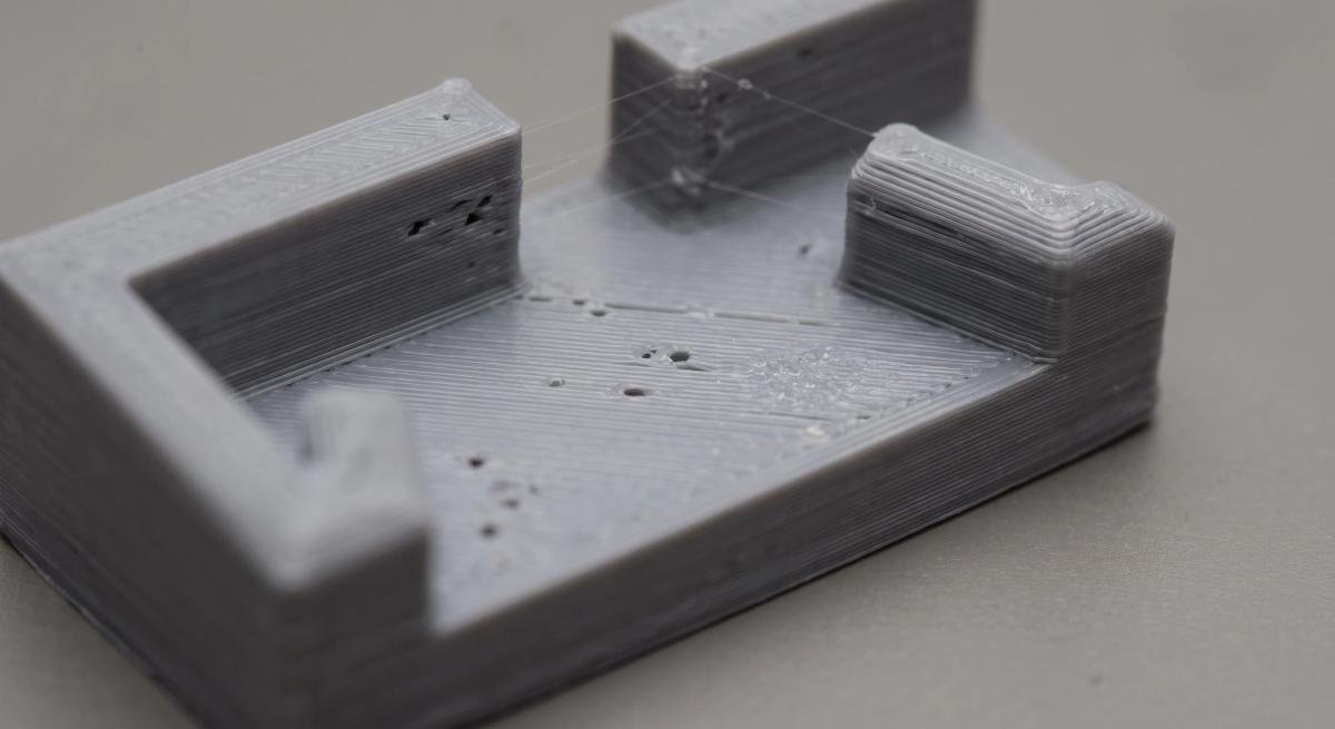 Macro view of a 3D printed surface showing scattered pinholes and thin stringing from slightly damp filament