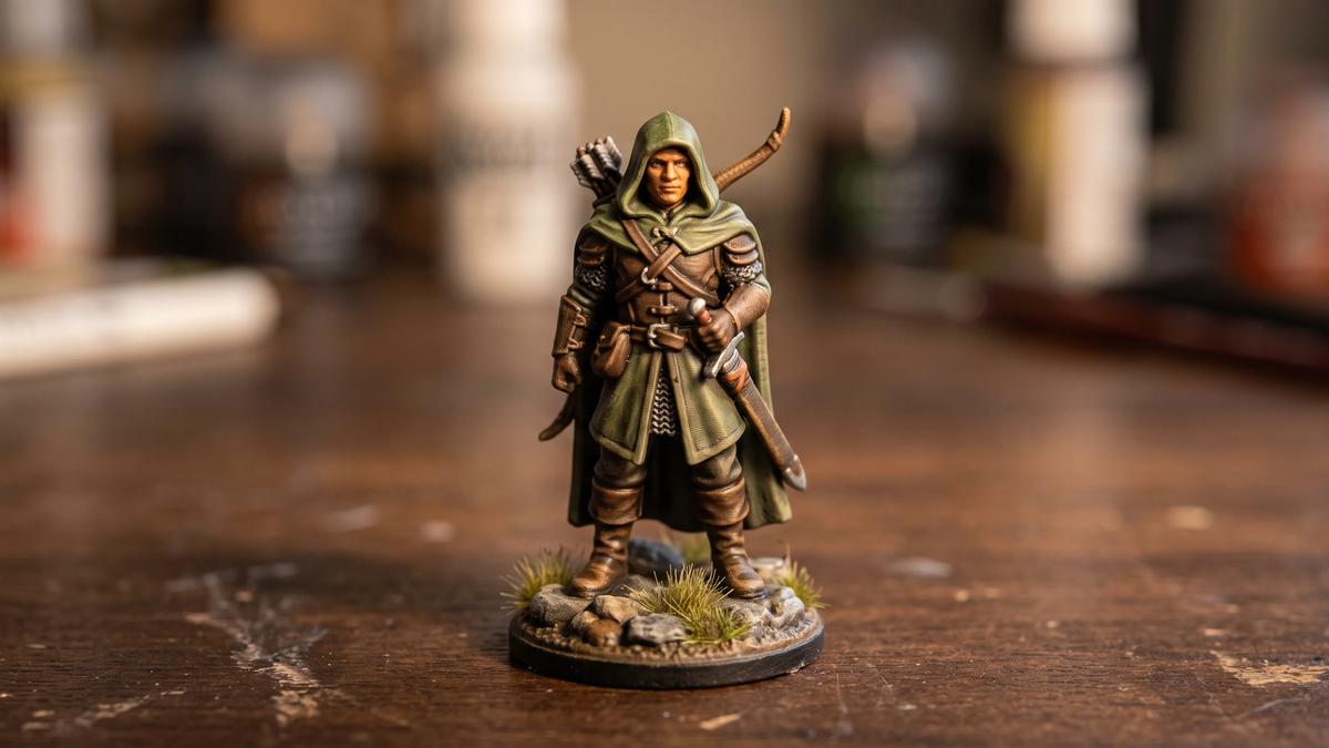 Painted 3D printed ranger miniature in a green hooded cloak standing on a textured base