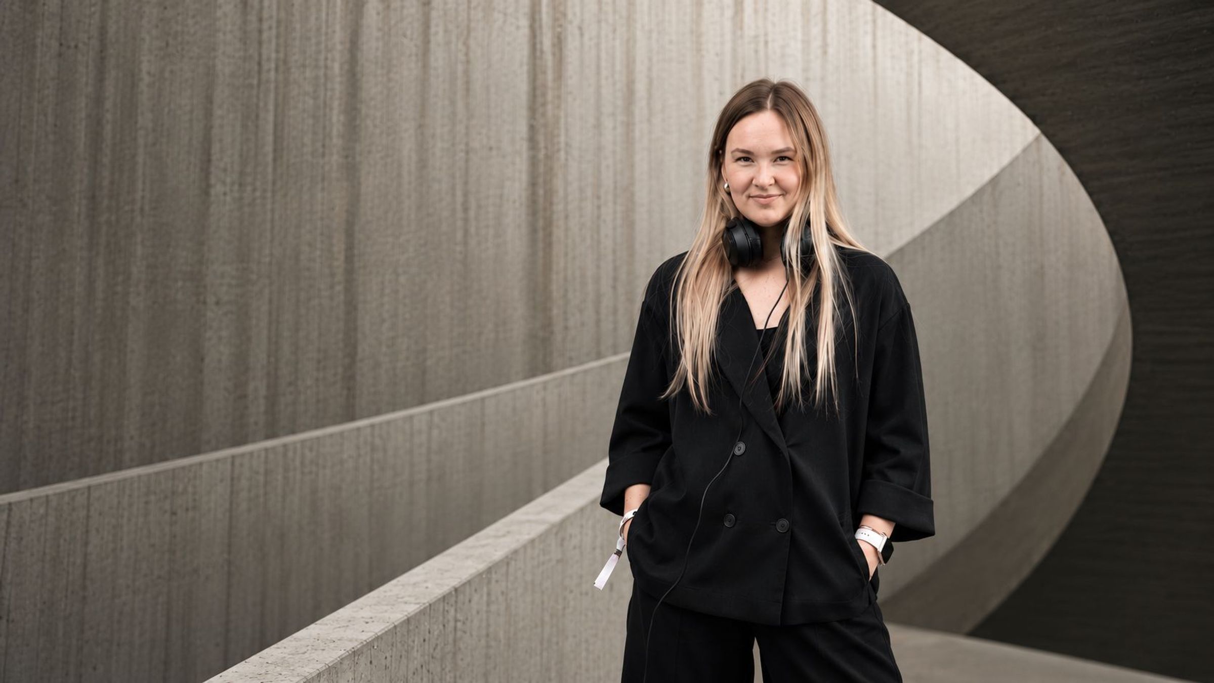 Anne Luhaäär-Mikk standing against a curved concrete wall, headphones around her neck.