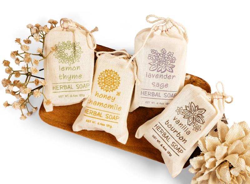 a variety of herbal soaps in cavnas bags on a wood tray with a white background for ecommerce photo