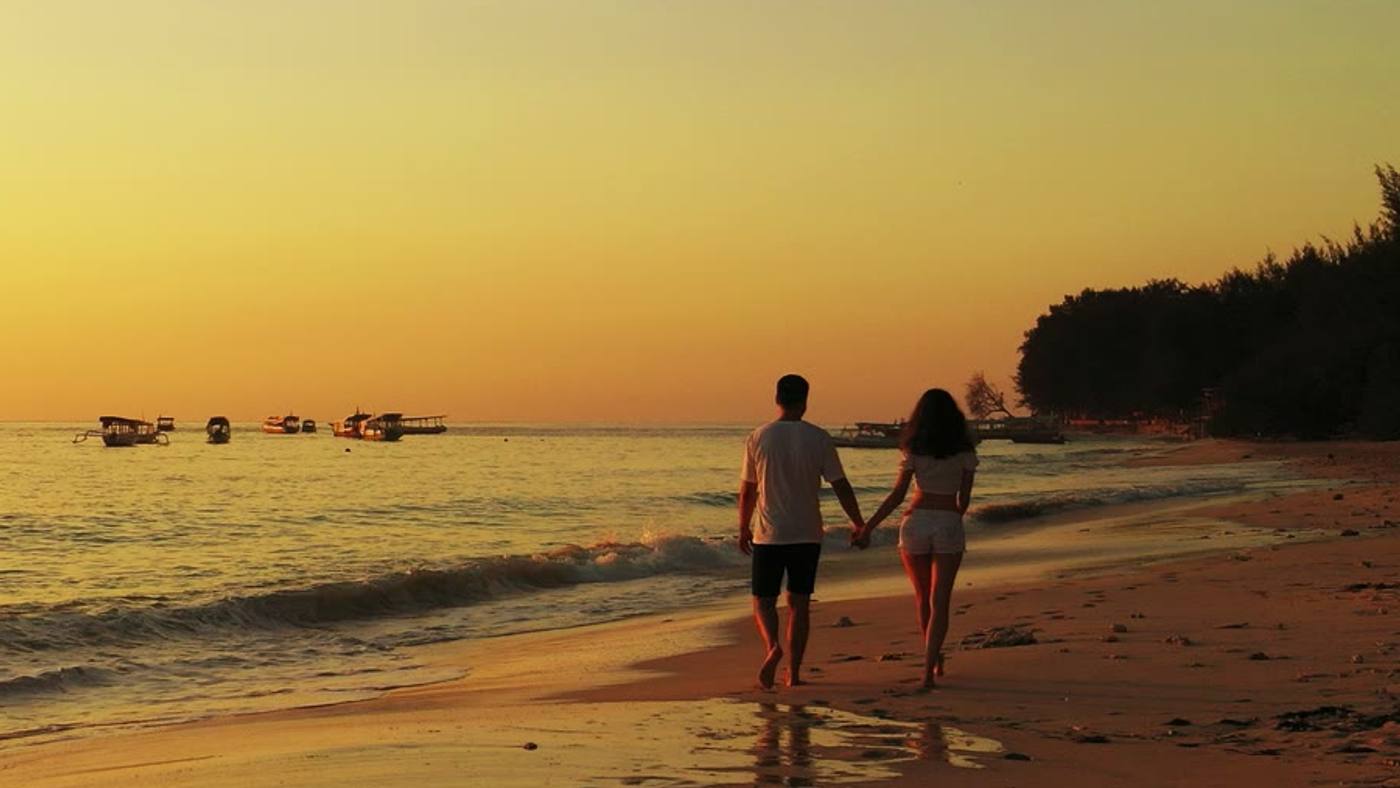 A couple walking hand in hand along the shore at sunset