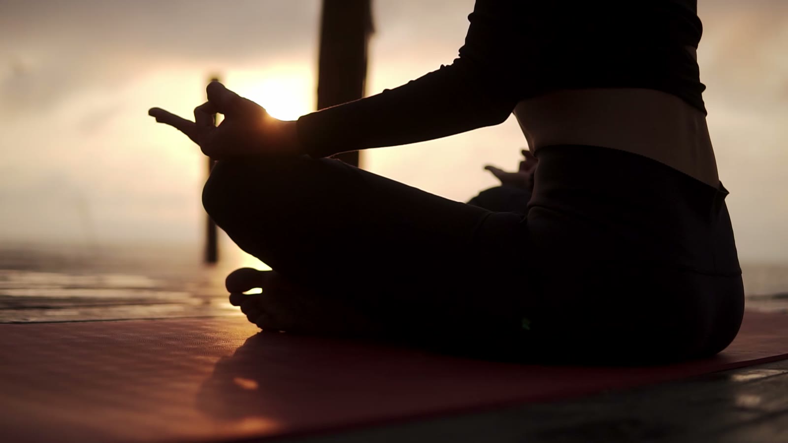 A seated meditation in silhouette at sunrise, the sun between the fingers