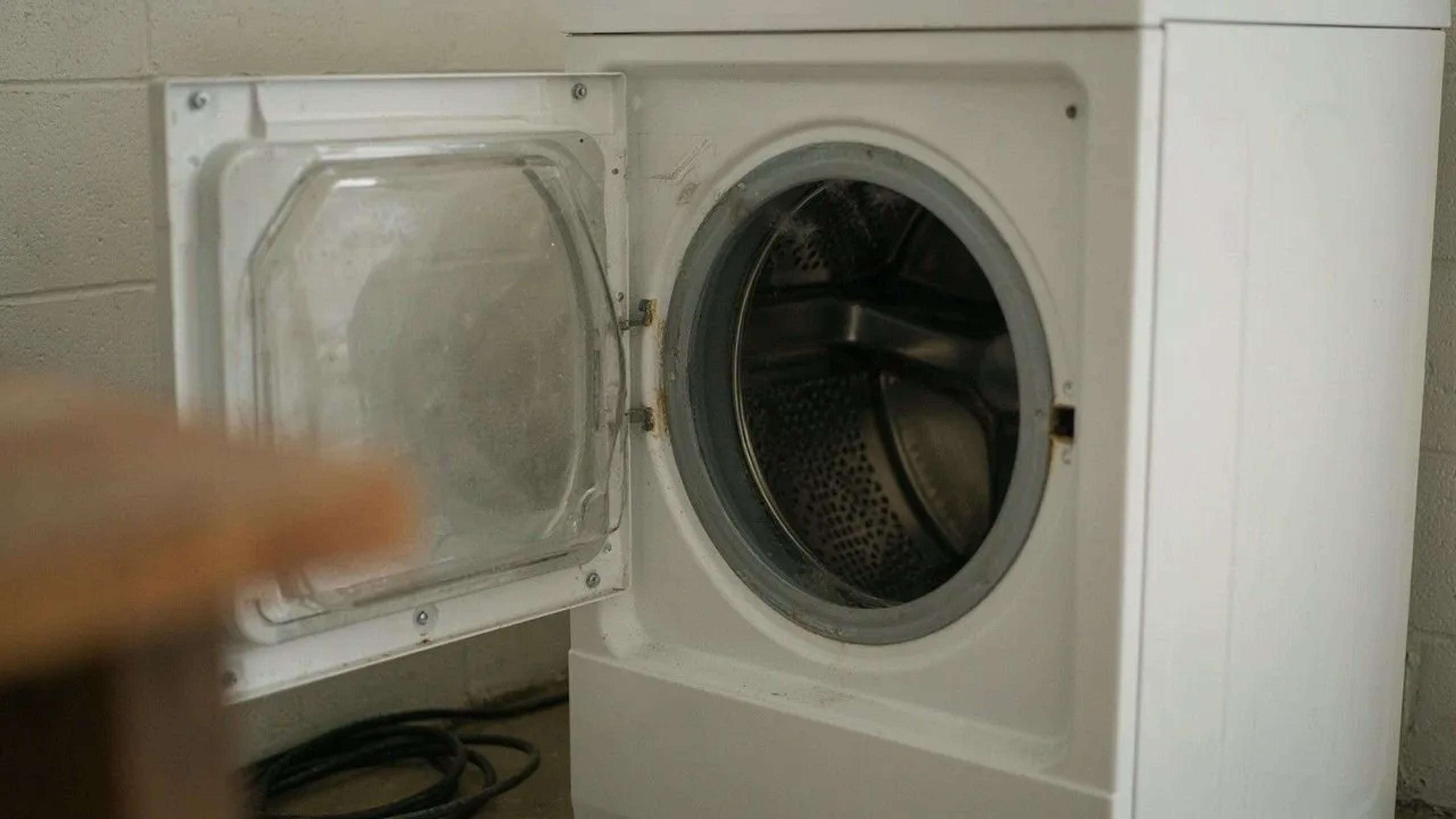 White front-loading laundry machine with its door open against a cinder block wall
