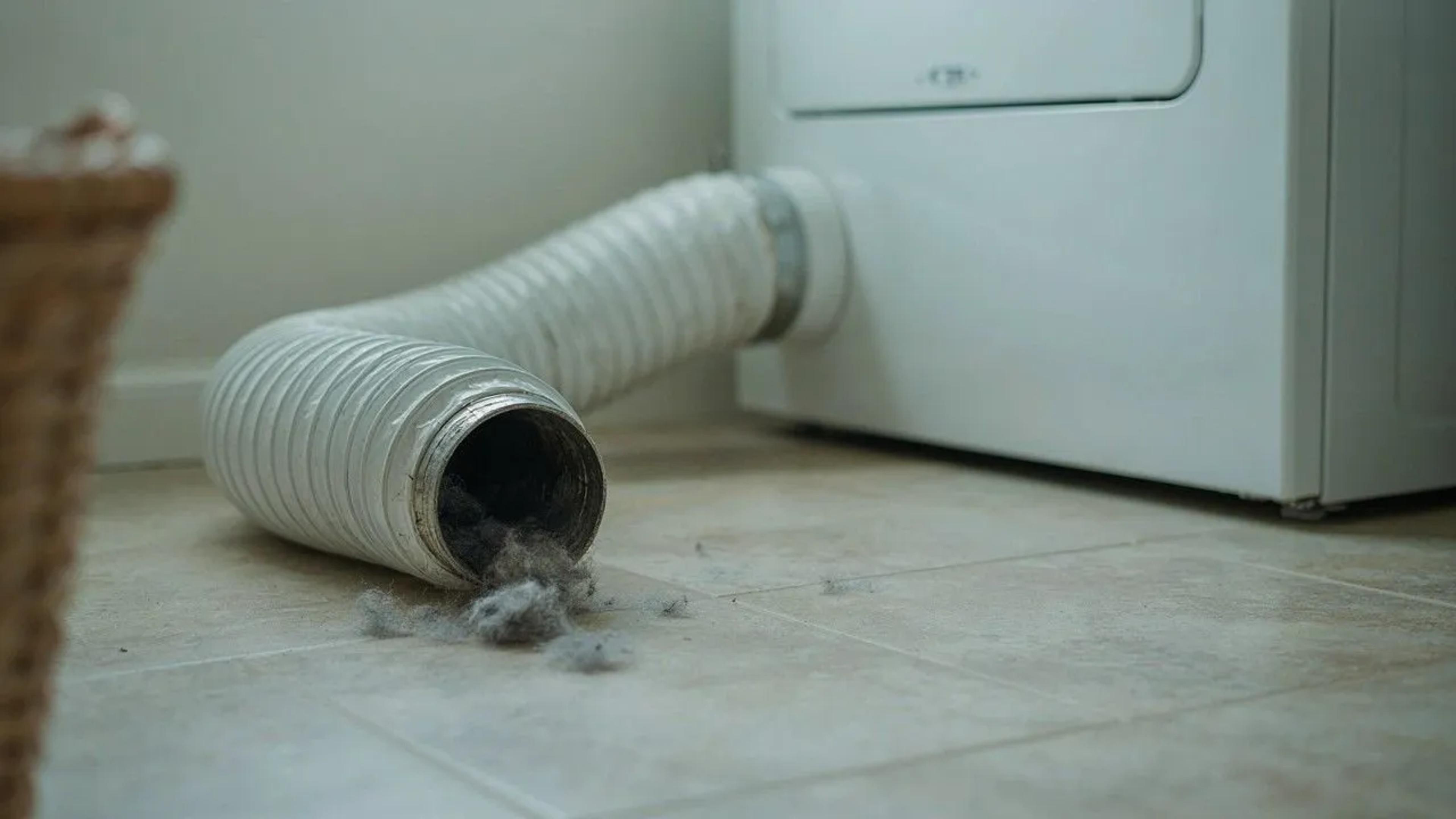Flexible white foil dryer vent hose detached from a dryer, with clumps of lint spilling out
