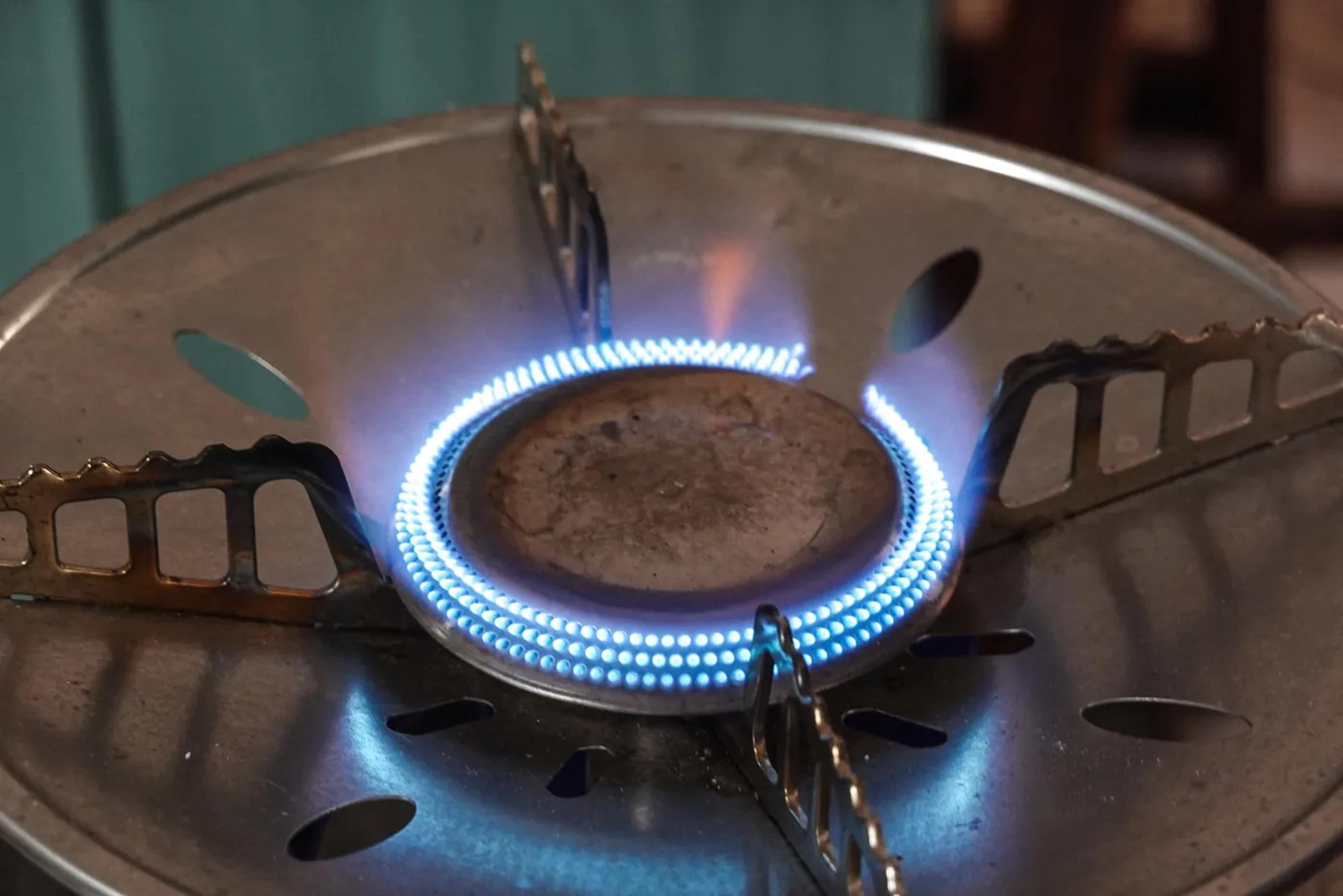 Close-up of a lit gas burner ring with small blue flames