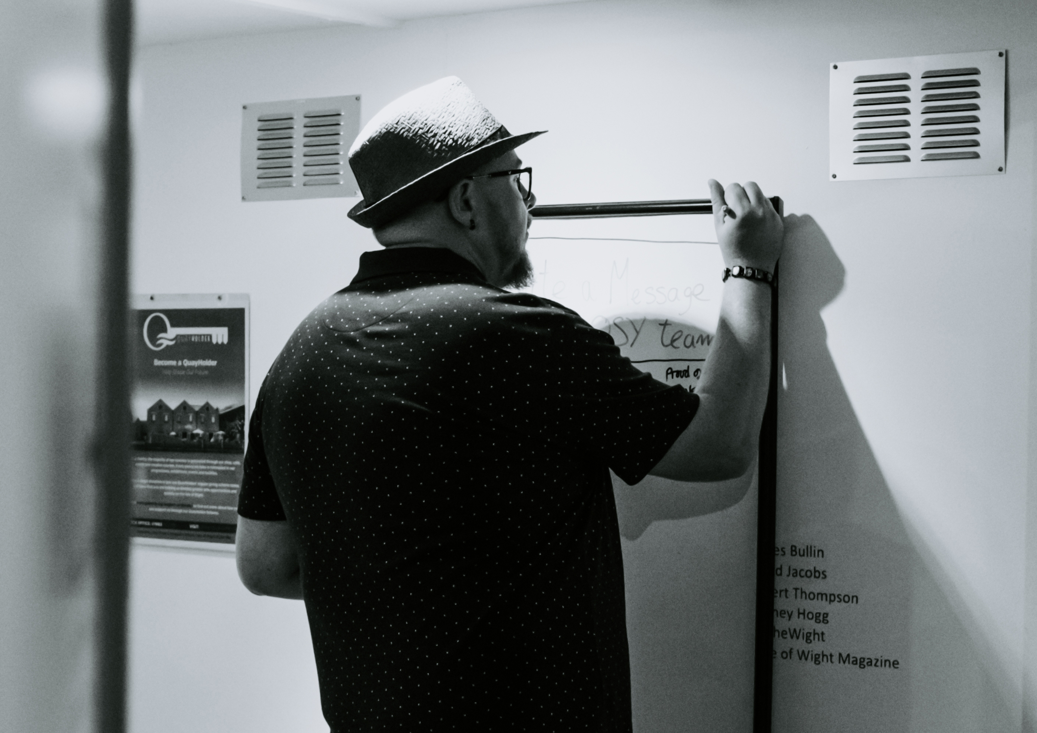 Scott Bennett wearing a fedora and writing on a wall-mounted board at the NOSY studio.
