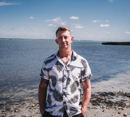 Professional headshot of Dan Carley, Client Director at NOSY Agency, wearing a white shirt with a seaside background.