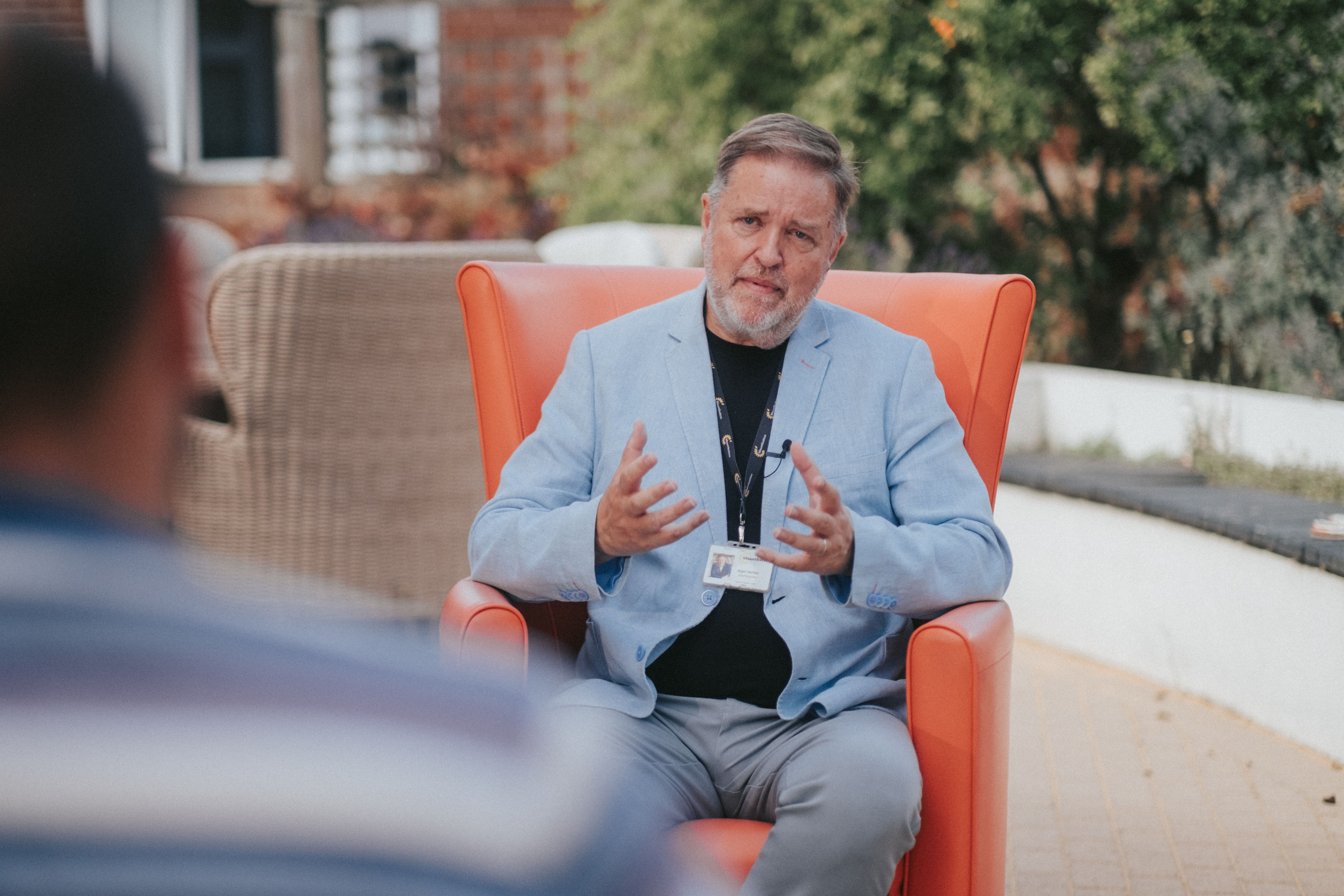 Hospice CEO talking to NOSY team member sitting in an orange chair in the hospice garden.