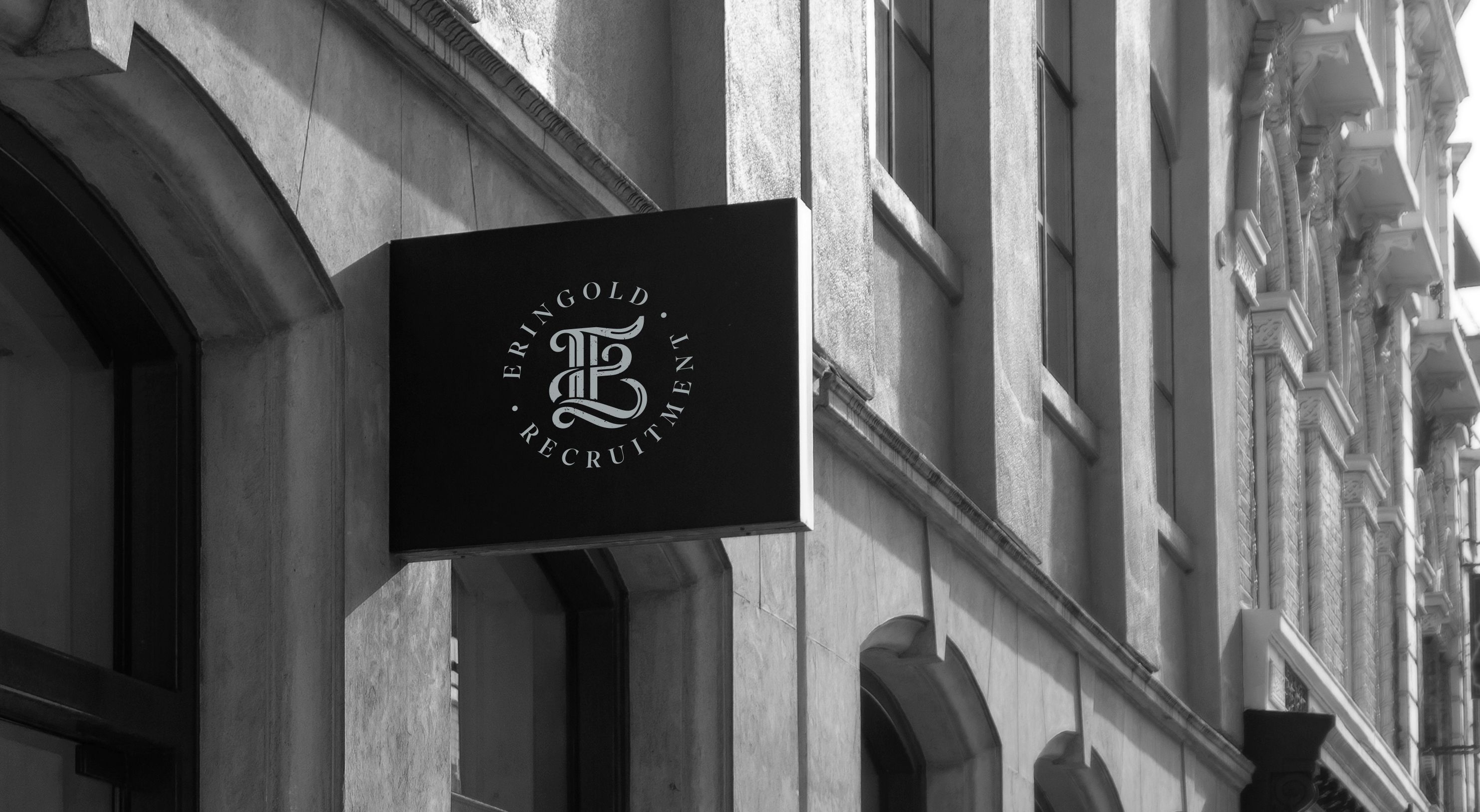  Eringold Recruitment sign with a silver monogram logo displayed on a black signboard outside a stone building.