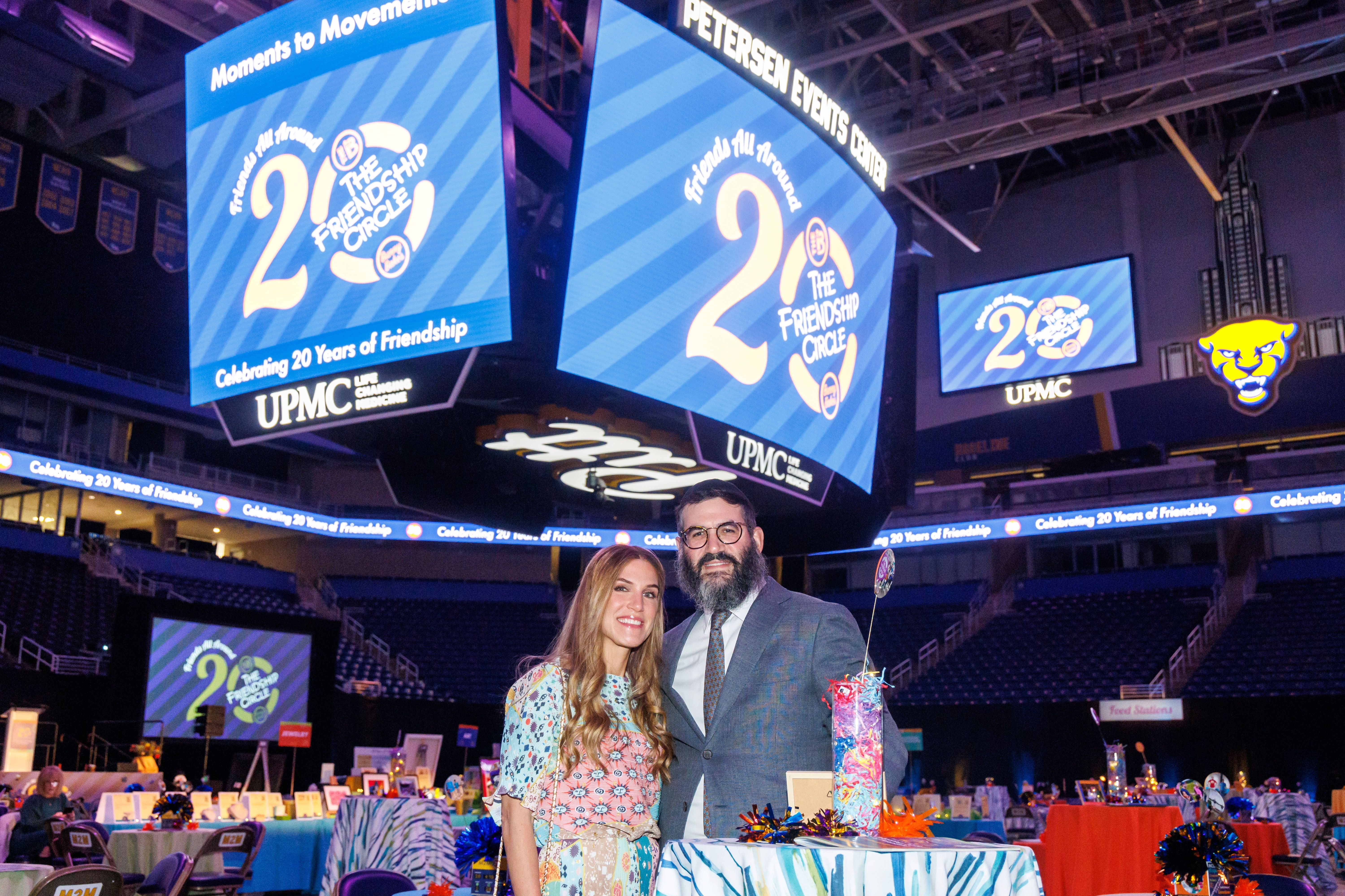 Friends All Around logo is on the Jumbotron at the Petersen Events Center, behind Rivkee and Rabbi Mordy Rudolph