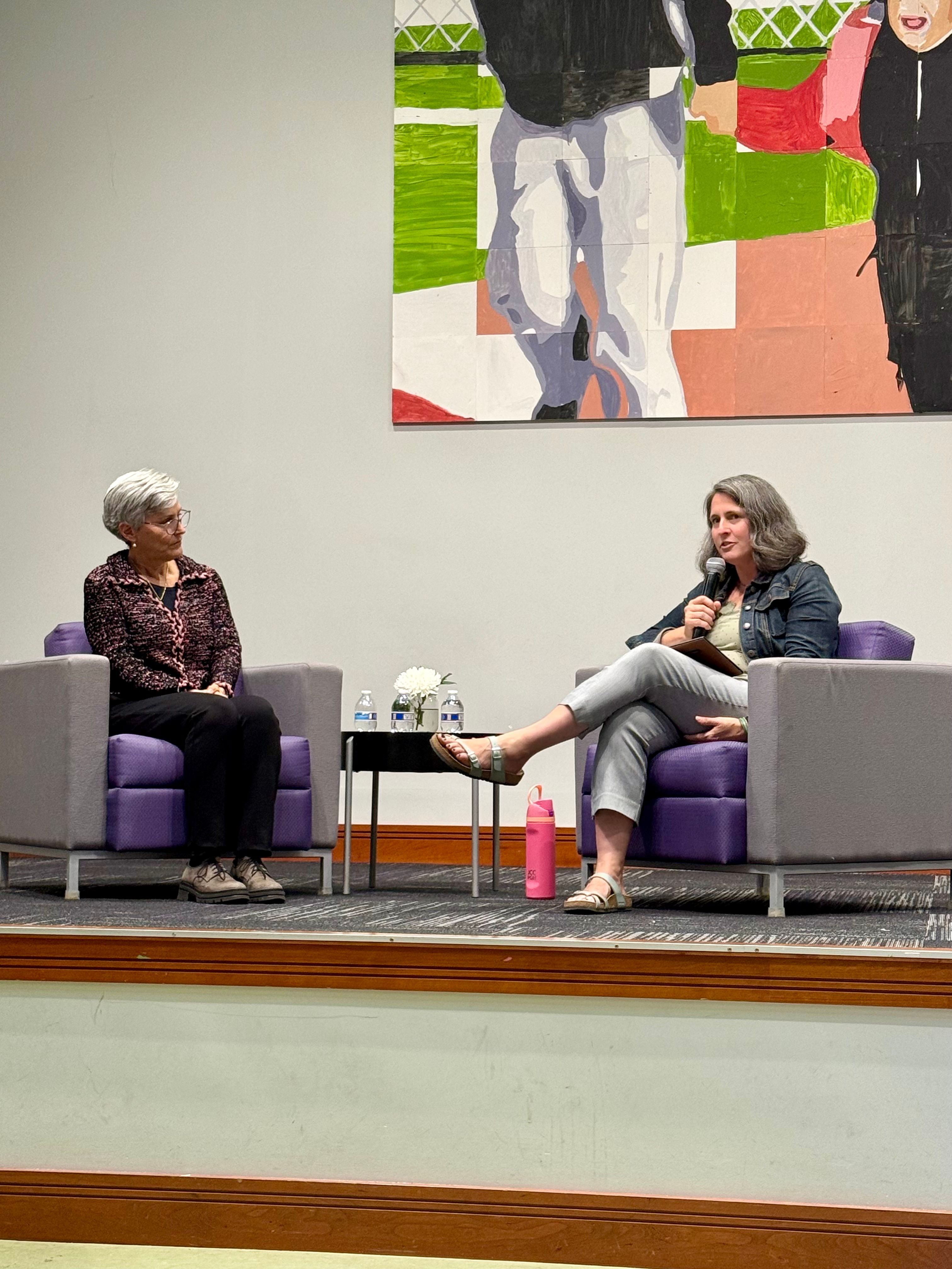 The two speakers are seated in chairs with microphones as they lead a community conversation on mental health, healing and support.