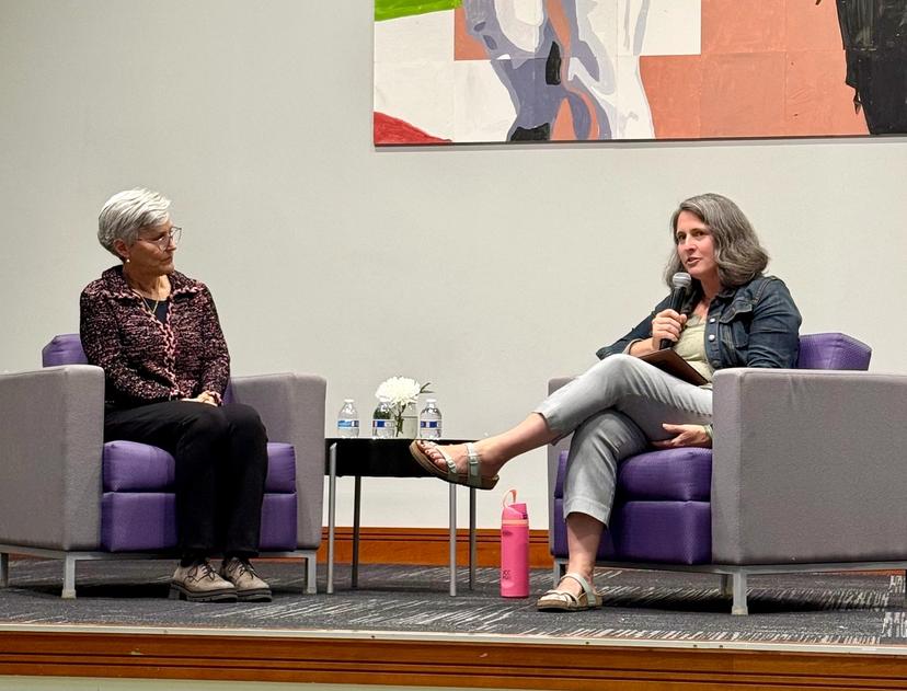 The two speakers are seated in chairs with microphones as they lead a community conversation on mental health, healing and support.