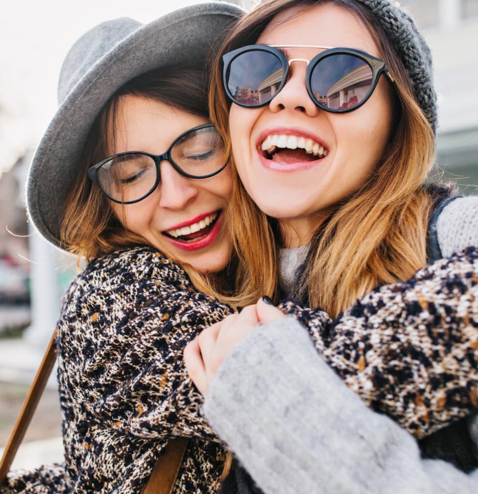 one lady in eyeglasses and one with sunglasses hugging each other