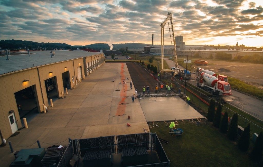 Crew finishing a large concrete pour beside an industrial building at sunset.