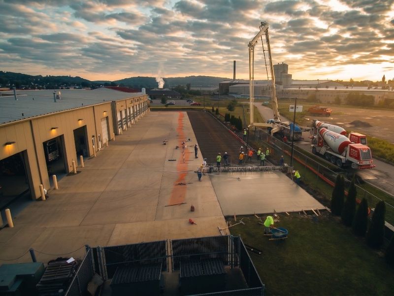 Crew finishing a large concrete pour beside an industrial building at sunset.