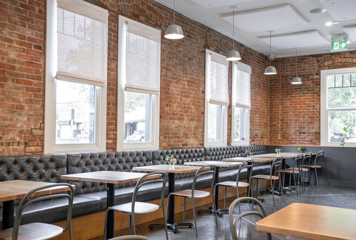 Bright and inviting dining room at Pip in Edmonton, featuring exposed brick walls, tufted leather banquette seating, large windows, and modern tables in a restored historic space.