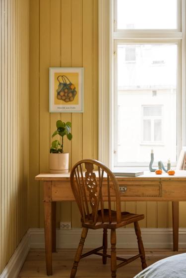 Pinnestol foran et antikt skrive bord i ett rom med sennepsgult malte paneler.