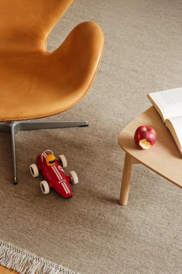 Bord, stol og lekebil på ett beige teppe.