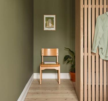 En stol står i en nisje i en klassisk leilighet i olivengrå fargetoner