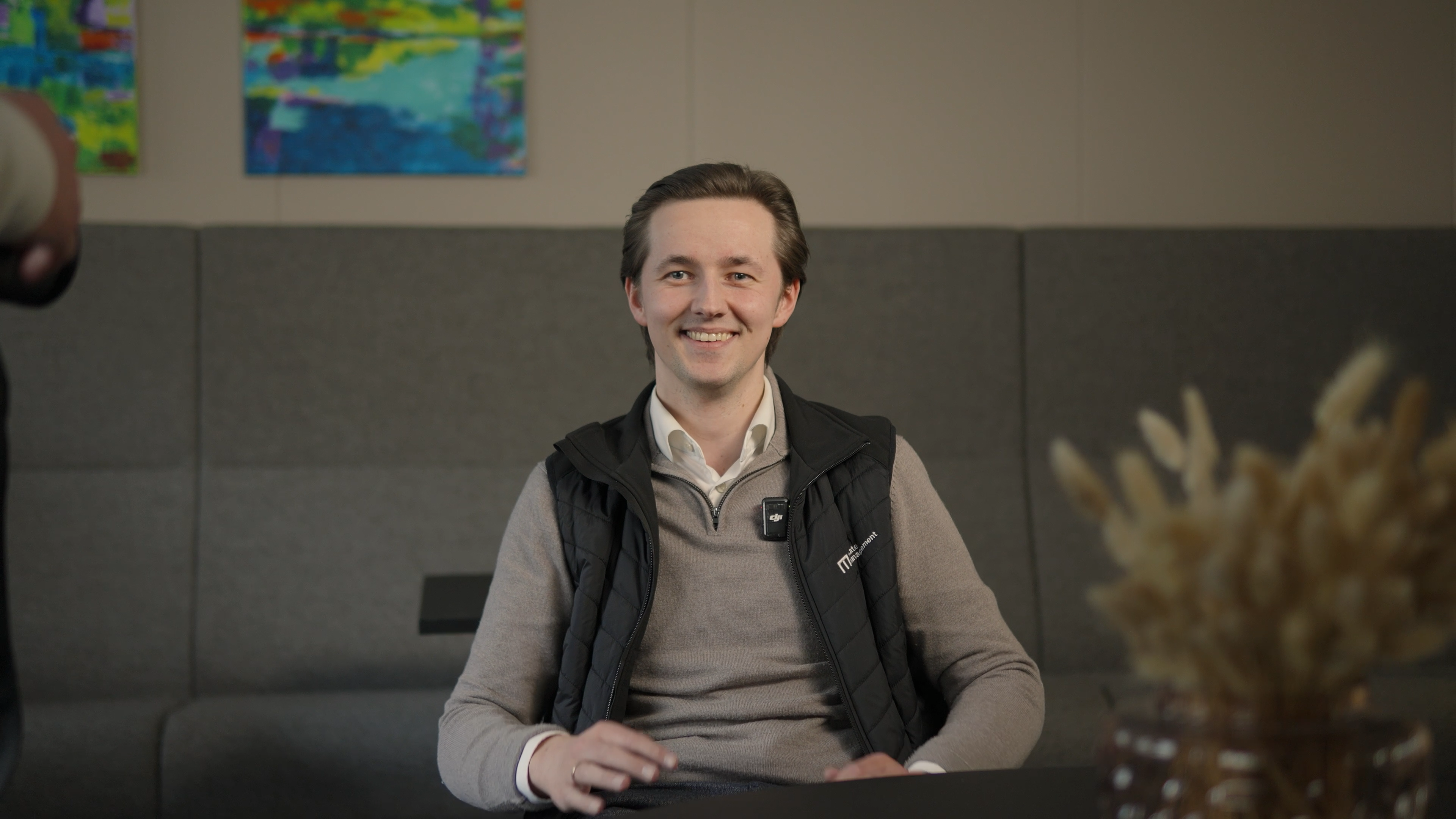 Mann smiler under videointervju, sittende på en stol med et bord foran seg