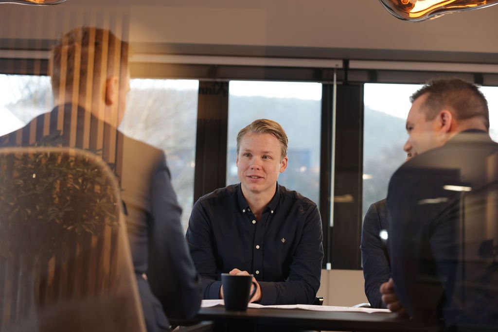 Tre menn rundt et bord hvor en person sitter mot kamera