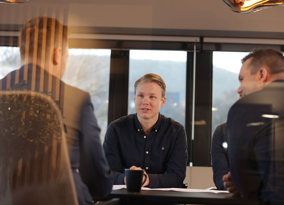 Tre menn rundt et bord hvor en person sitter mot kamera