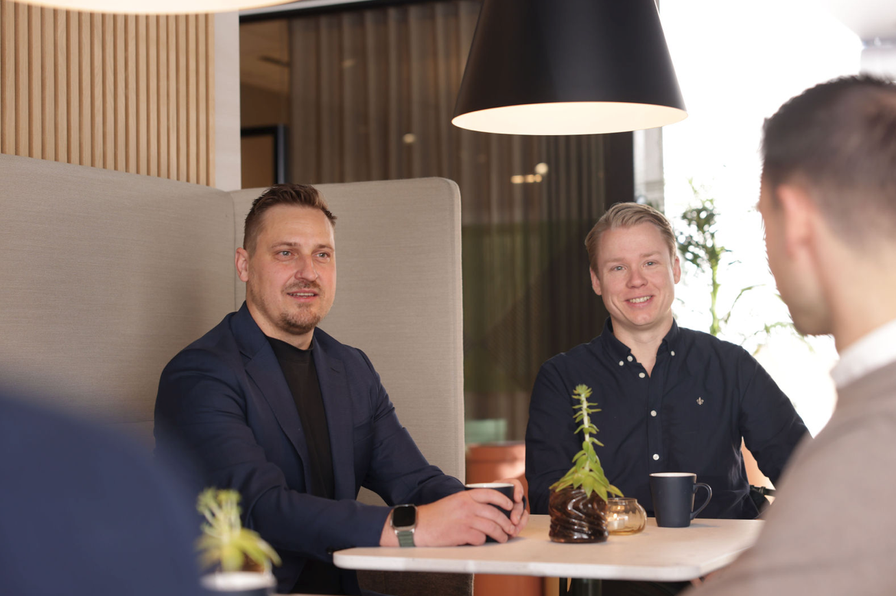 Tre ansatte rundt et bord nyter en kopp kaffe