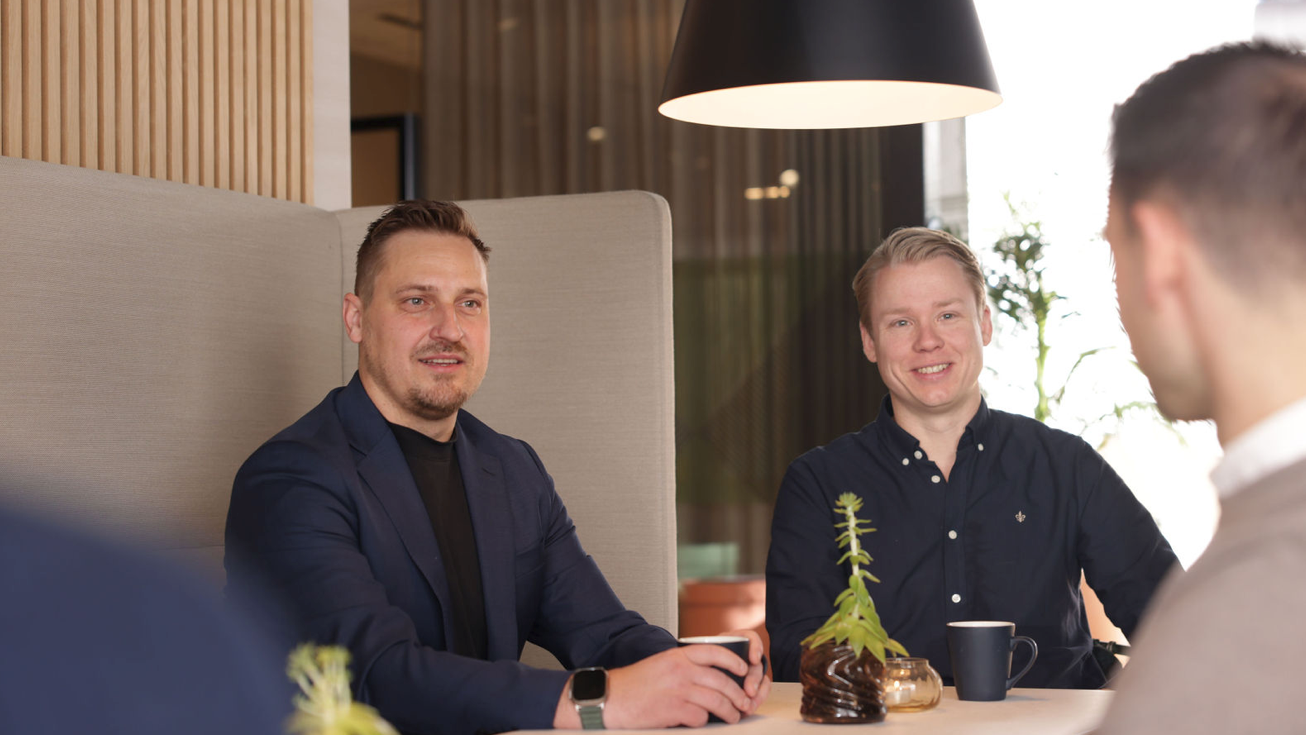 Tre ansatte rundt et bord nyter en kopp kaffe